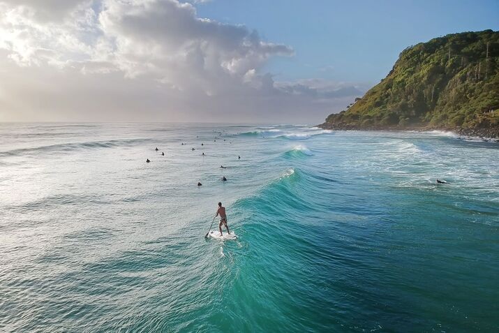Paddleboarder riding a wave at Burleigh Heads, capturing the spirit of a peaceful yet active Gold Coast adventure along the coastline.
