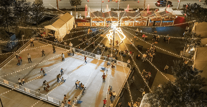 Aerial view of an outdoor ice-skating rink and festive market at night, with families skating under string lights as part of Christmas gold coast events